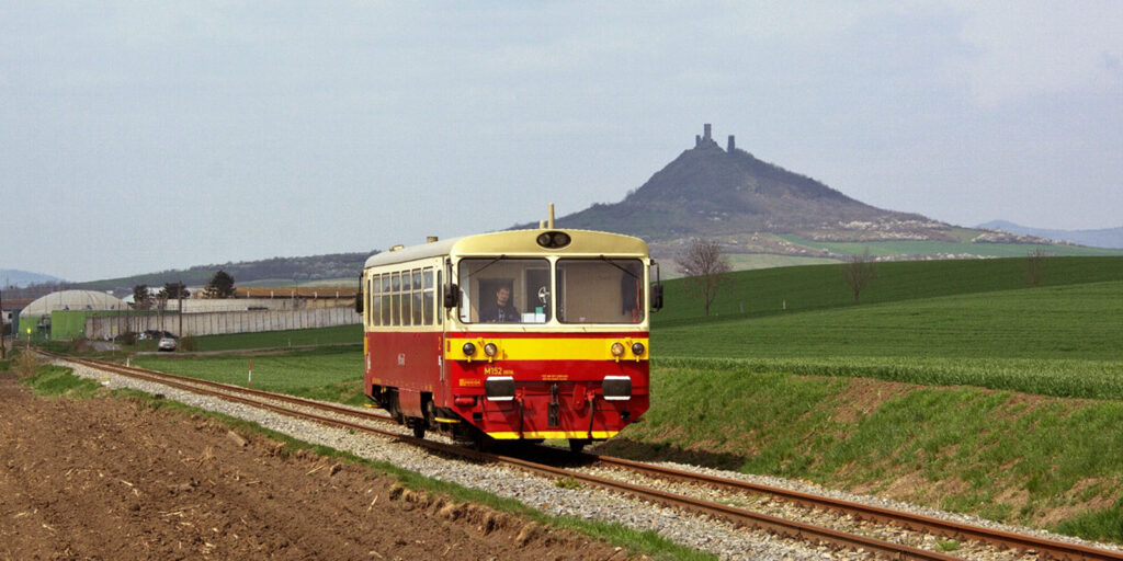 Podřipský motoráček projíždí pod hradem Hazmburk v Českém středohoří.